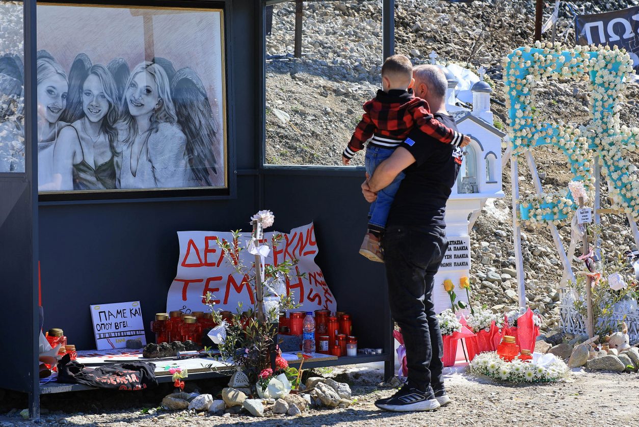 Εικόνα που δείχνει πατέρα με παιδί μπροστά σε πορτρέτο των αδικοχαμένων διδύμων και της ξαδέλφης τους που επέβαιναν στο μοιραίο τρένο